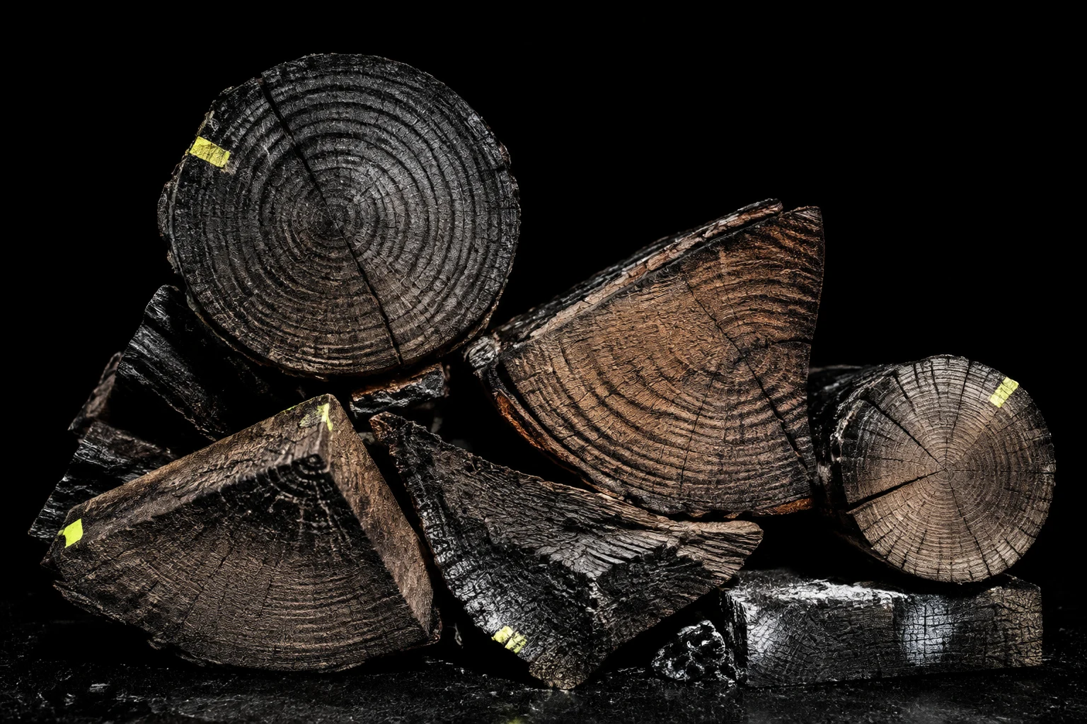 A sculptural arrangement of charred split timber with small acid-yellow index marks